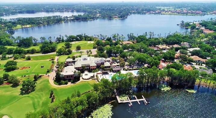 A historic clubhouse at the Isleworth Golf Course, surrounded by lush greenery and tall trees, offering a charming and peaceful ambiance for golfers